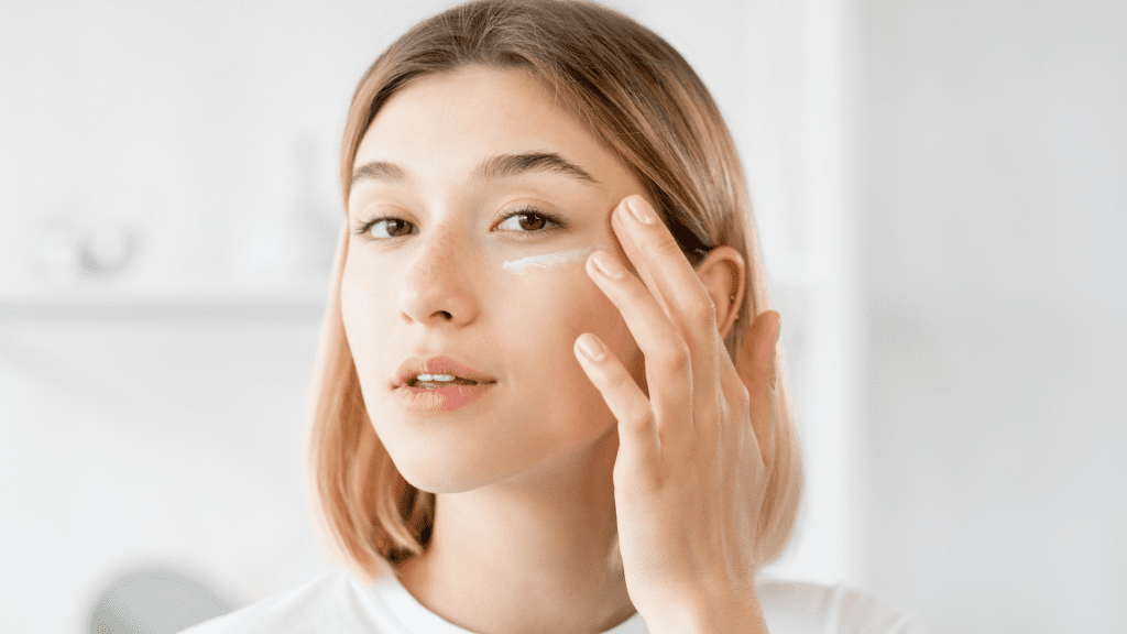 Young woman applying skincare cream under her eye with her finger.
