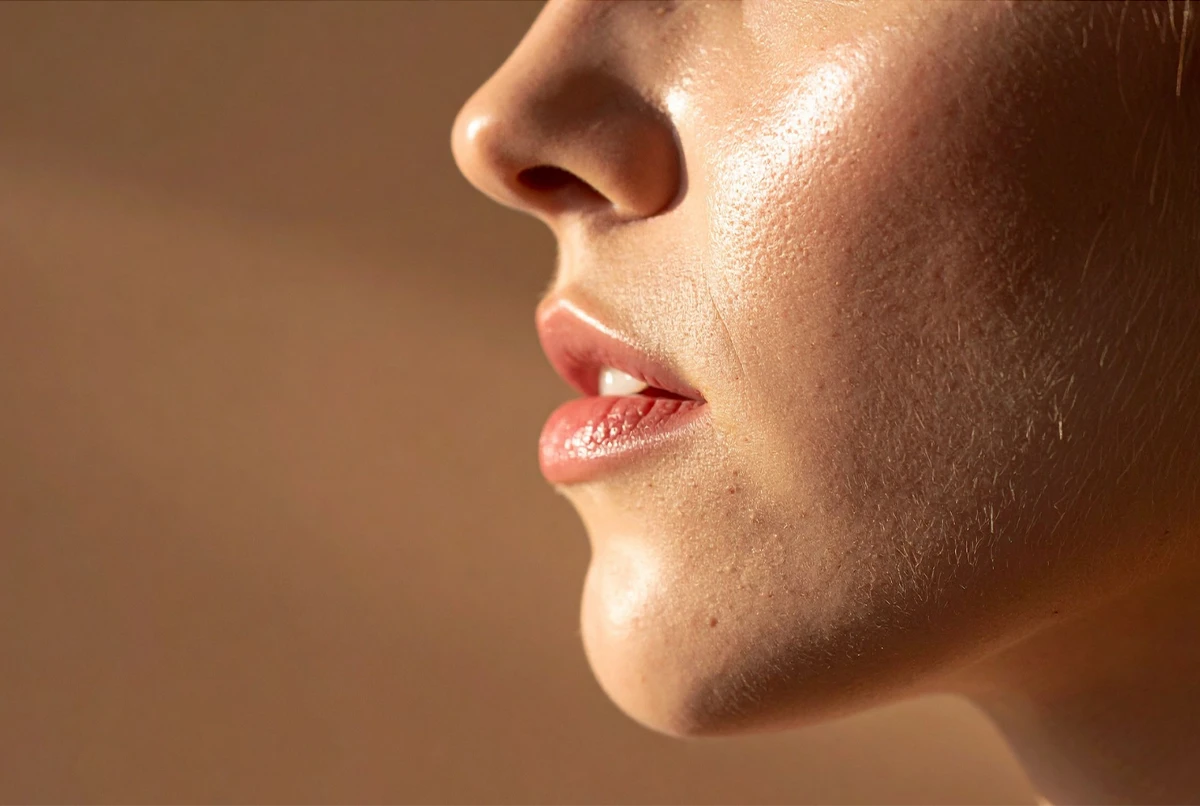 Close-up of a person's profile showing lips, chin, and nose against a neutral background