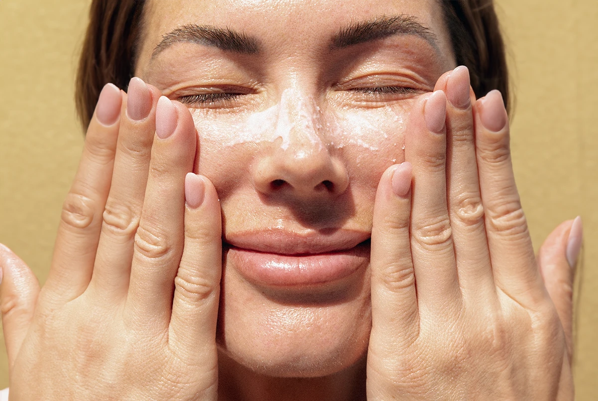 Person with closed eyes applying facial cleanser with both hands