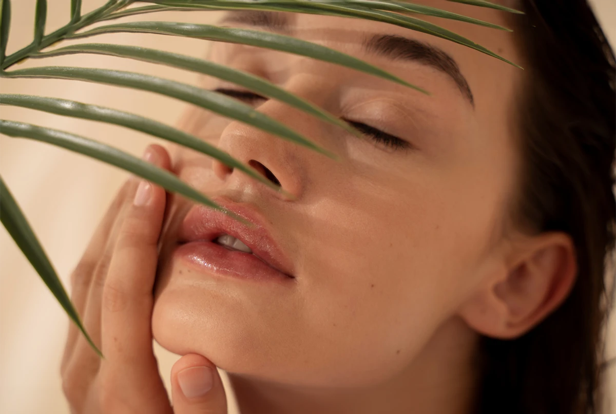 Close-up of a person gently touching their face, partially obscured by a leaf