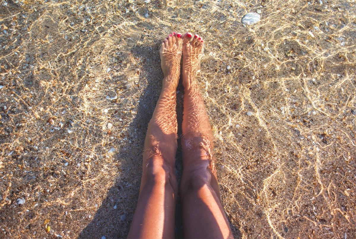 Legs and feet submerged in clear water, with pebbles visible beneath the surface