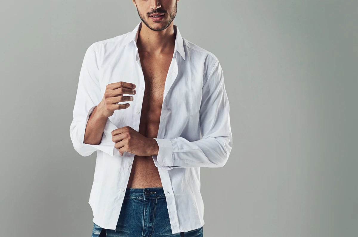 Man in a white open shirt and jeans, adjusting his sleeve. Gray background