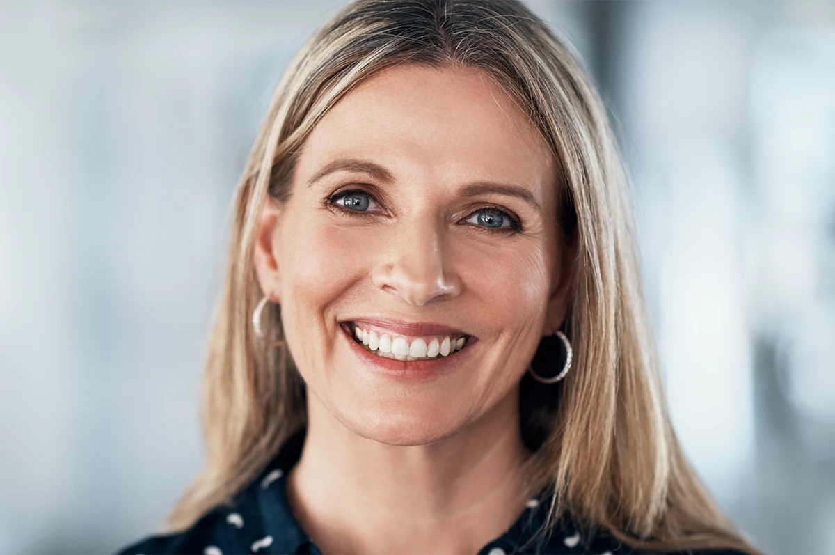Smiling woman with long blonde hair, wearing hoop earrings and a patterned shirt