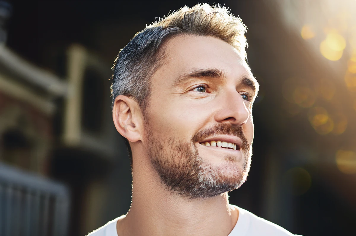 Man with short gray hair and a beard, smiling and looking to the side