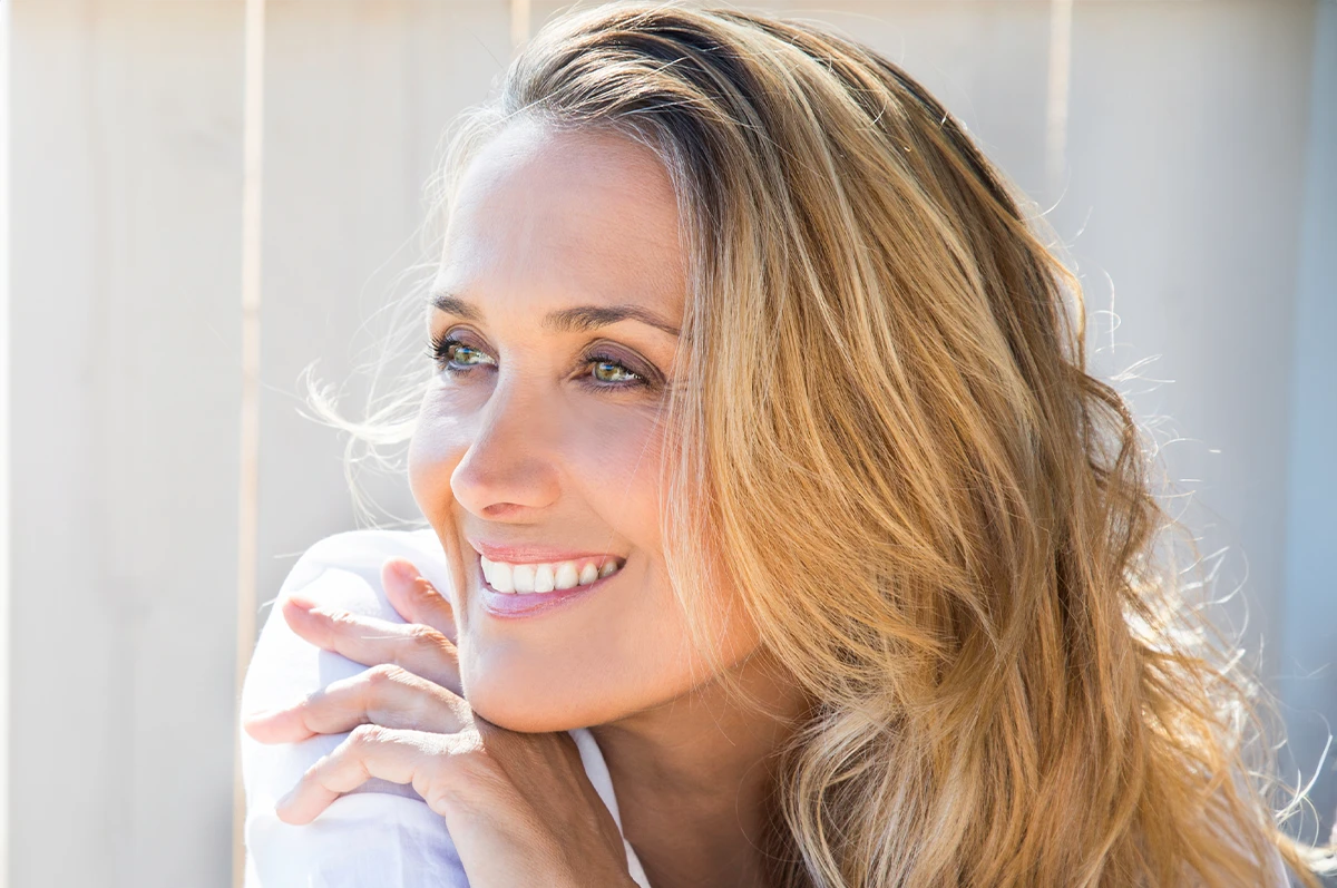 A woman with long, wavy hair smiling and resting her chin on her hands