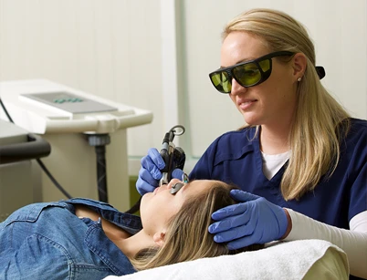 A clinician with gloves uses a laser on a patient lying down in a treatment room