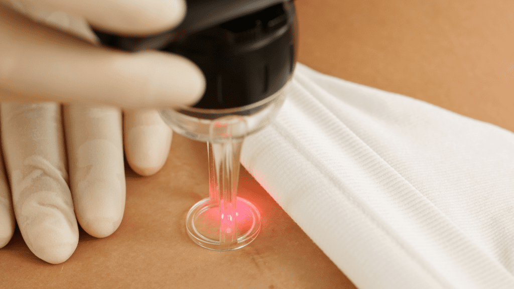 A hand wearing a glove holds a device emitting a red laser on skin