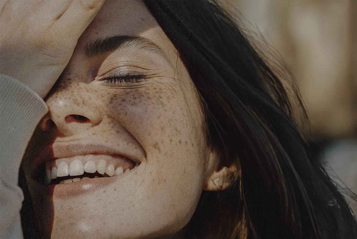 Close-up of a woman smiling, showing freckles and eyes closed in joy