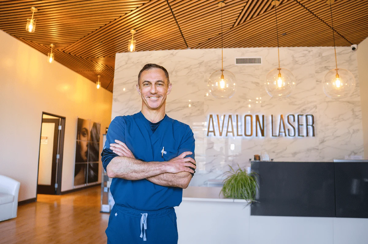 A man stands smiling with arms crossed in a modern interior with lights and a reception desk