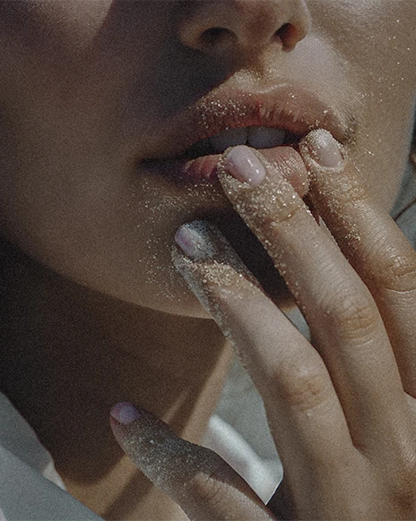 Close-up of a woman's face with sandy fingers near her lips