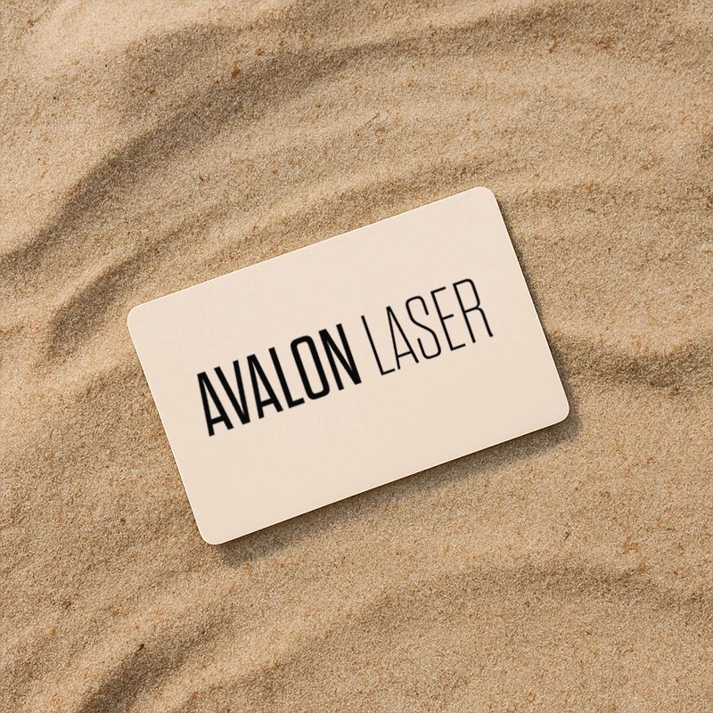 A plain card on sand displaying the text "AVALON LASER."